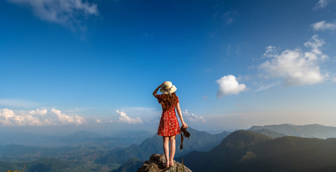 Woman hand holding camera and standing on top of the rock in nature. Travel concept.